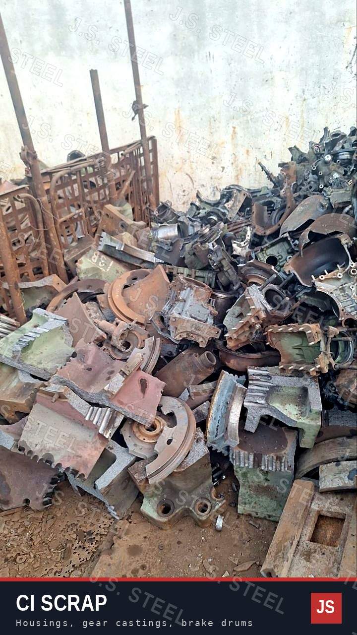 CI scrap lot: cast iron gearbox housings, gear castings and brake drums against a yard wall, J.S. STEEL Bhavnagar